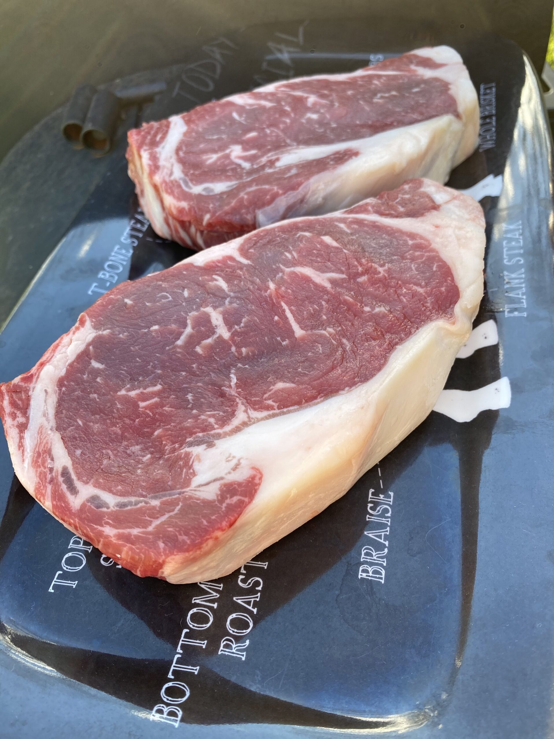Two raw ribeye steaks displayed on a black platter, showcasing marbling and thickness, ideal for grilling or roasting.